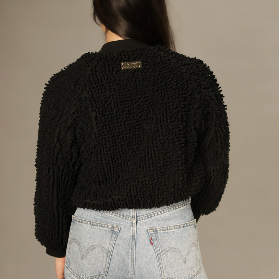 Model wearing the SHAGBAGG black shag bomber jacket in a front angled view with hands in pockets and gold zipper.