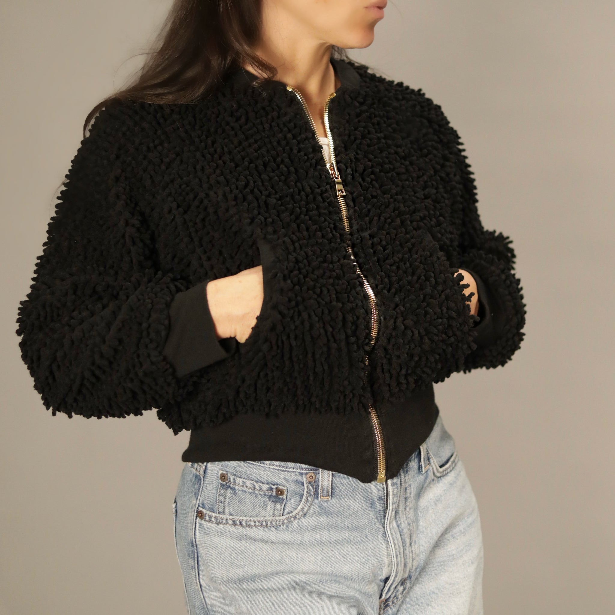 Model wearing the SHAGBAGG black shag bomber jacket in a front angled view with hands in pockets and gold zipper.