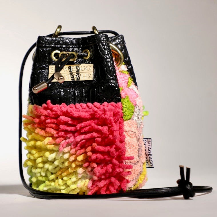 Multicolored textured bucket bag with black leather accents on a light gray background